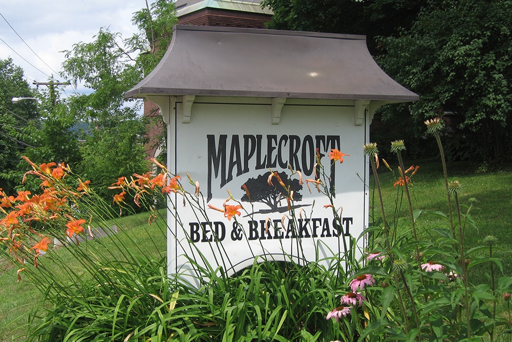 Maplecroft sign in spring, tiger lilies and daisies around the bottom of the sign