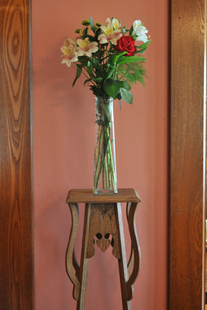 Rose and Lillies in glass vase on wooden plant stand against rose colored wall